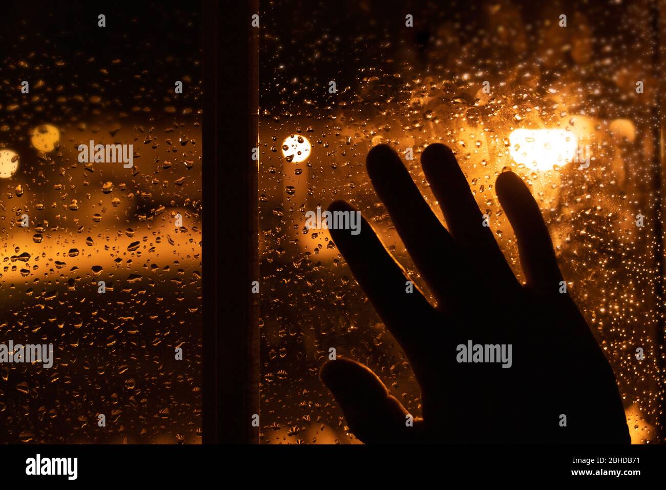 Silhouette of a hand leaning against the window on a rainy day at night. Sad image of melancholy looking out. Stock Photo
