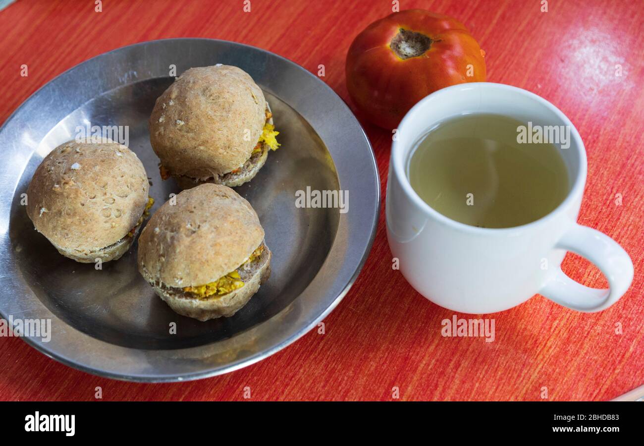 a simple healthy breakfast with three wheat rolls with curried eggs in a stainless steel plate and sour sop leaf herbal tea in a white mug Stock Photo