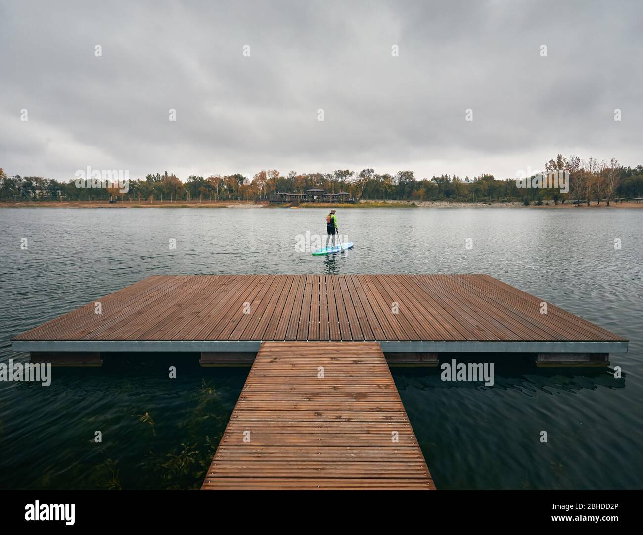 Athlete in wetsuit on paddleboard exploring the lake at cold weather