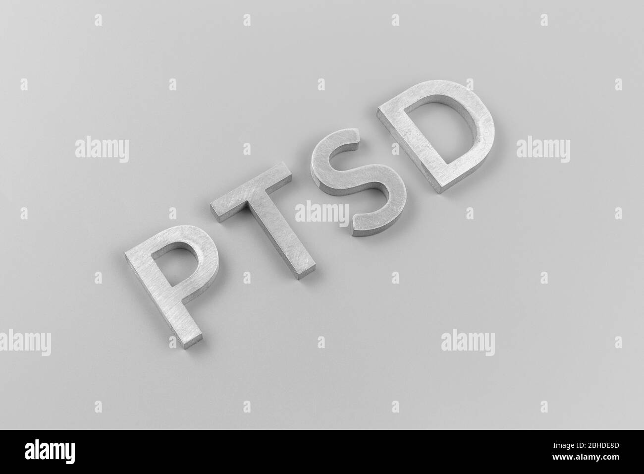 an abbreviation PTSD - post traumatic stress disorder - laid with silver metal letters on light gray flat surface Stock Photo