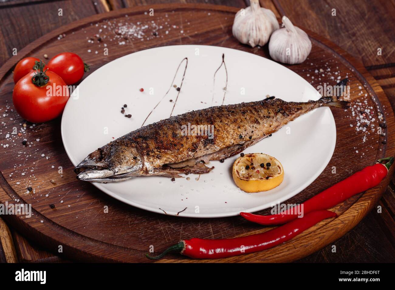 Appetizing mackerel fish baked on fire with spices, served on a plate and decorated with vegetables on wooden background Stock Photo