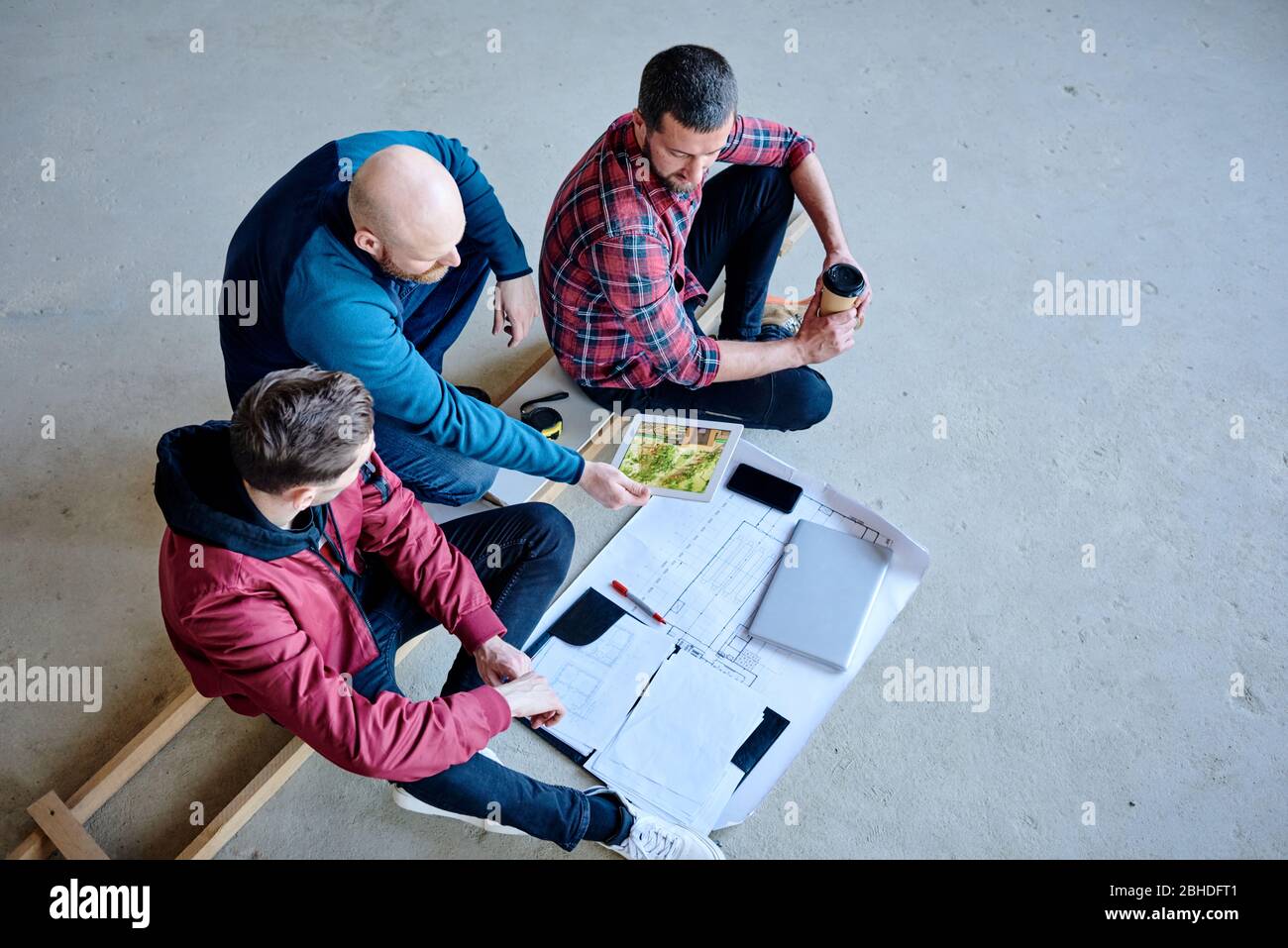 One of young builders showing his colleagues exterior of finished house in touchpad during discussion of furnishing materials at meeting Stock Photo