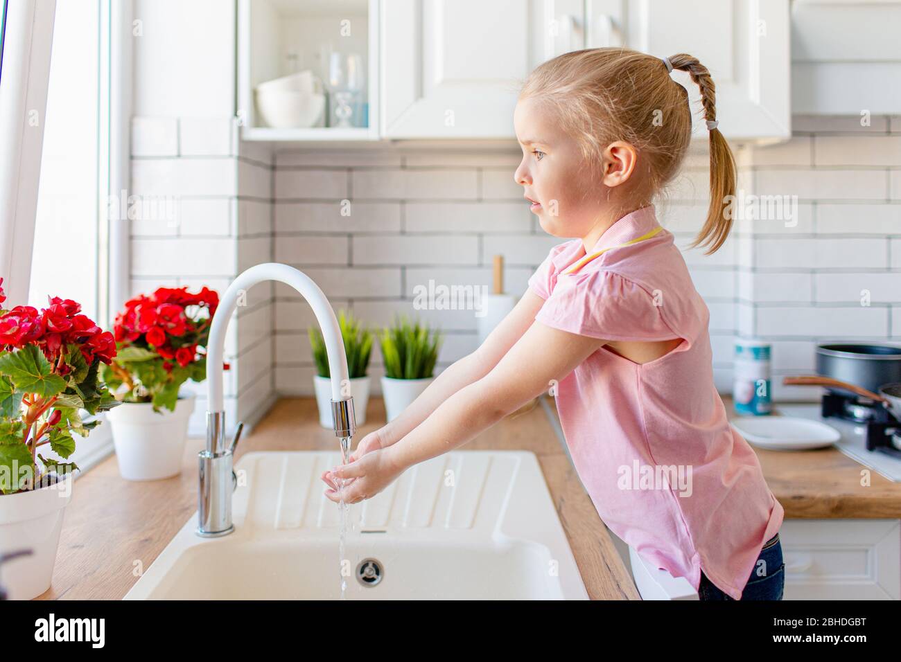 Blonde toddler girl washing hands in the lingh kitchen before eating. Hygiene and healthcare concept Stock Photo