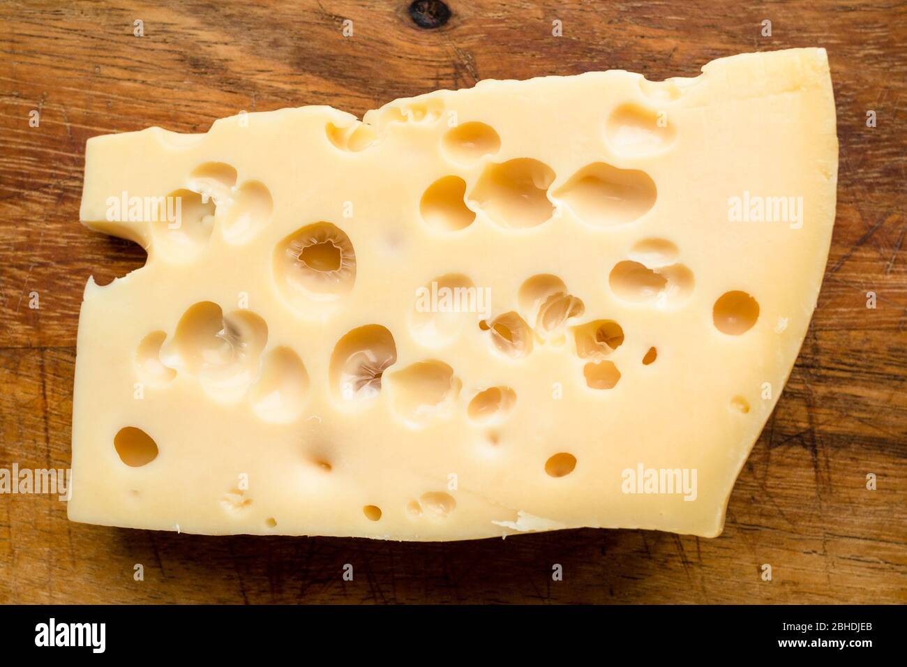 piece of yellow swiss cheese on wooden cutting board close up Stock Photo