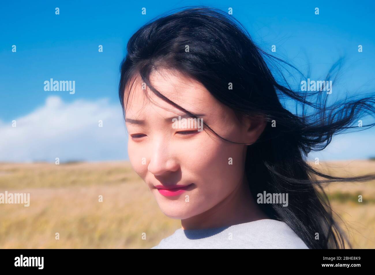 A chinese woman with hair blowing in the wind within the national seashore scenic area in Cape Cod Massachusetts on a sunny blue sky day. Stock Photo
