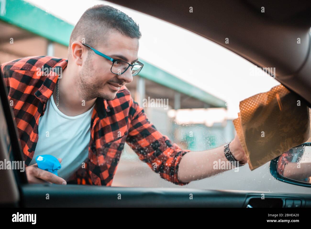 Young man cleaning the windows on his car with microfiber cloth. Stock Photo