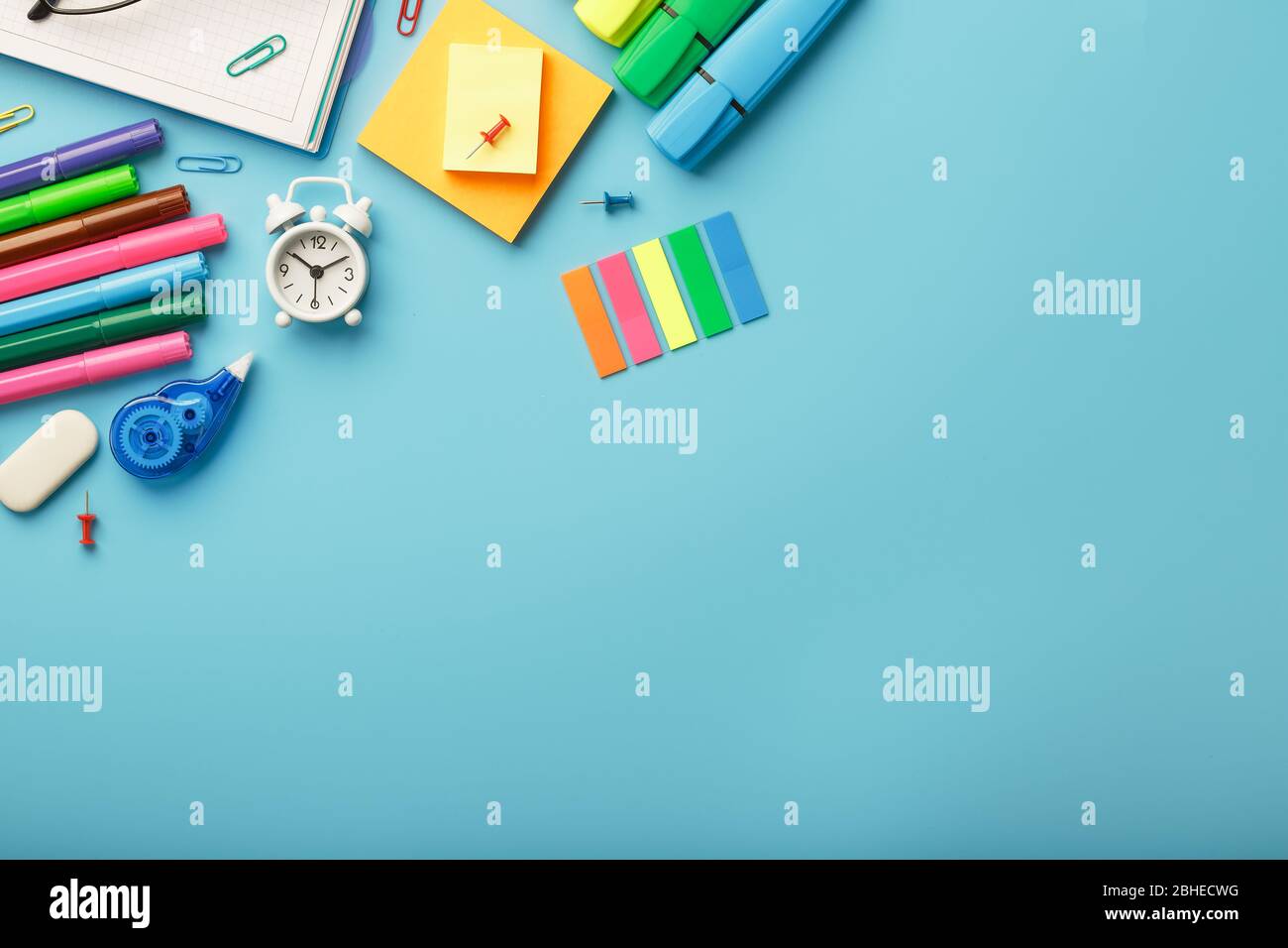 Colorful Stationery items with an alarm clock lie on a blue background ...