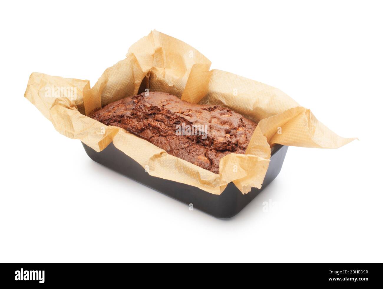 Studio shot of a chocolate fudge cake in a paper lined baking tin cut out against a white background - John Gollop Stock Photo