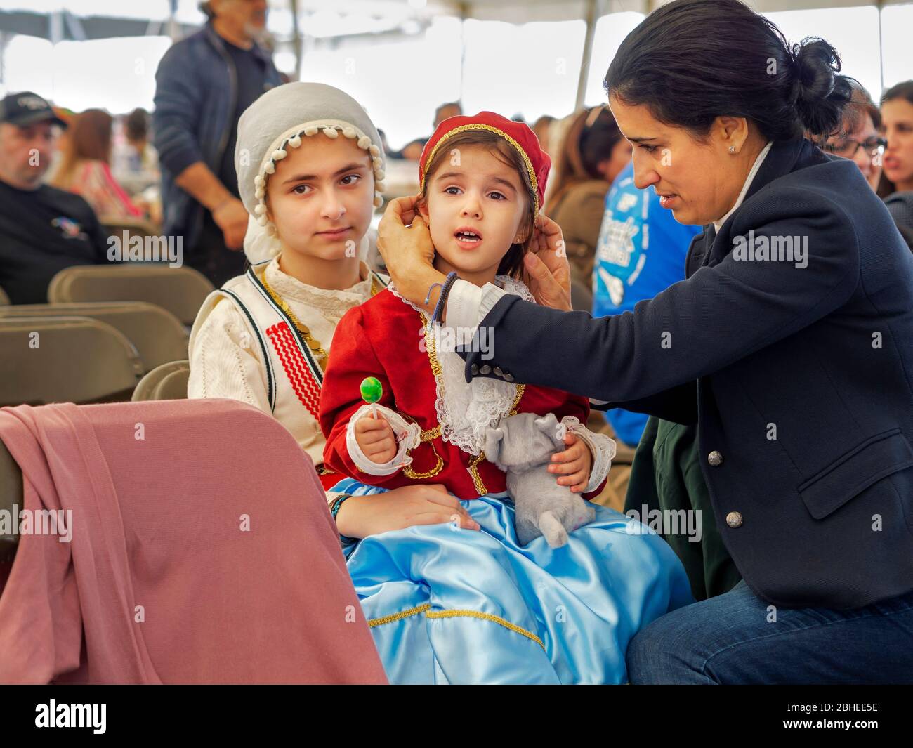 A woman adjusts the bonnet of the younger of two girls dressed in Greek costume at the 2019 Greek Festival in Corpus Christi, Texas USA. Stock Photo