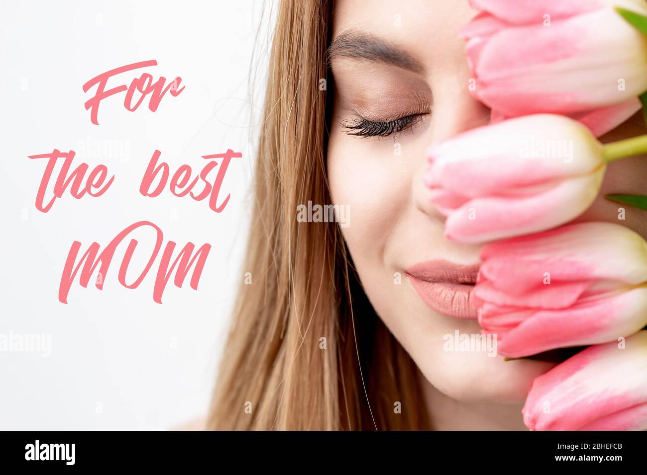 Smiling young woman with pink tulips, sign text For The Best Mom on white background. Mother's day celebration card. Stock Photo