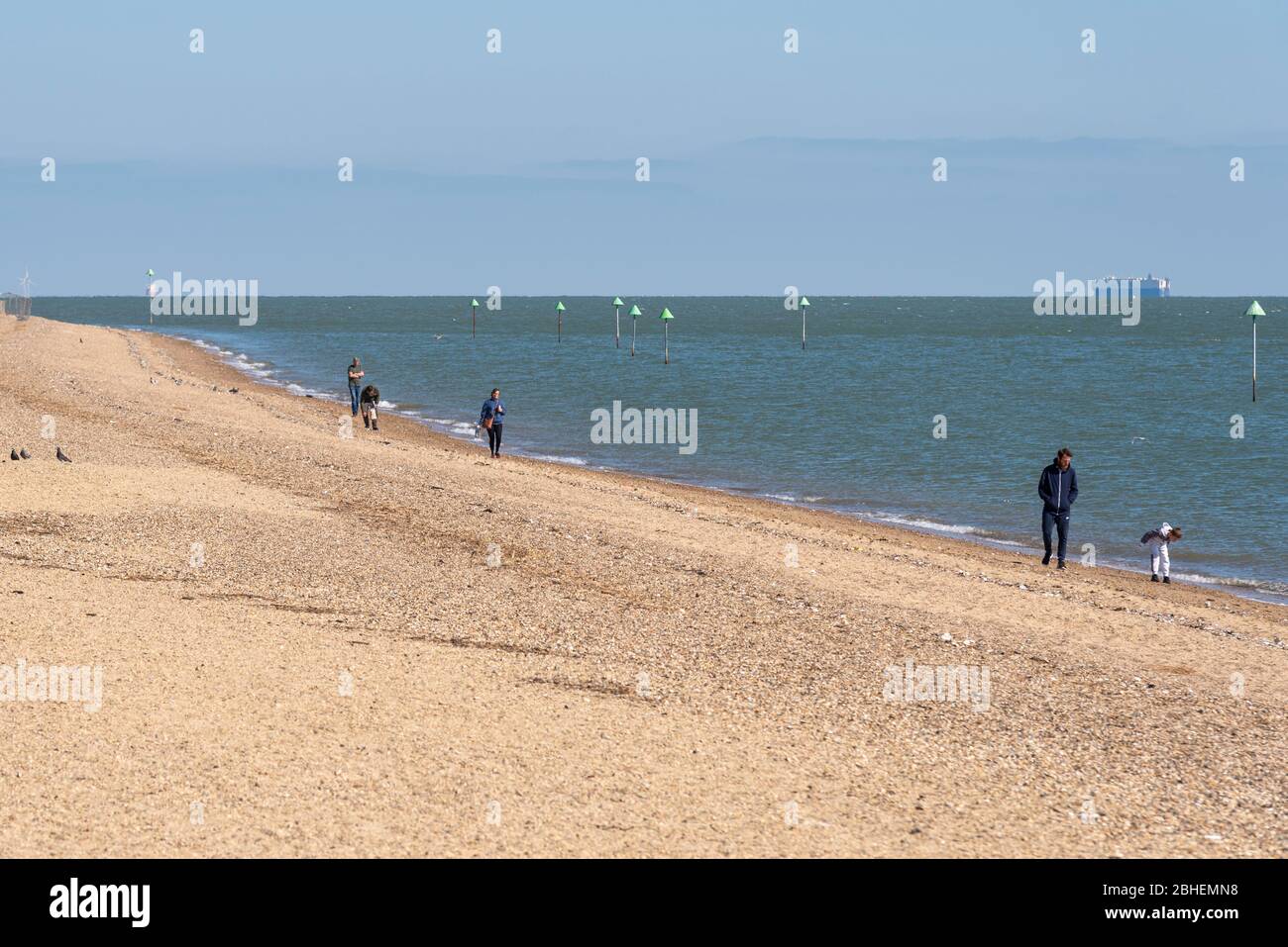 Southend on Sea, Essex, UK. 25th Apr, 2020. A few people are out enjoying the warm sunny weekend day in Southend on Sea but are largely obeying the request to stay home during the COVID-19 Coronavirus pandemic lockdown period. Those that are out are keeping to the social distancing guidelines, such as those walking the beach Stock Photo