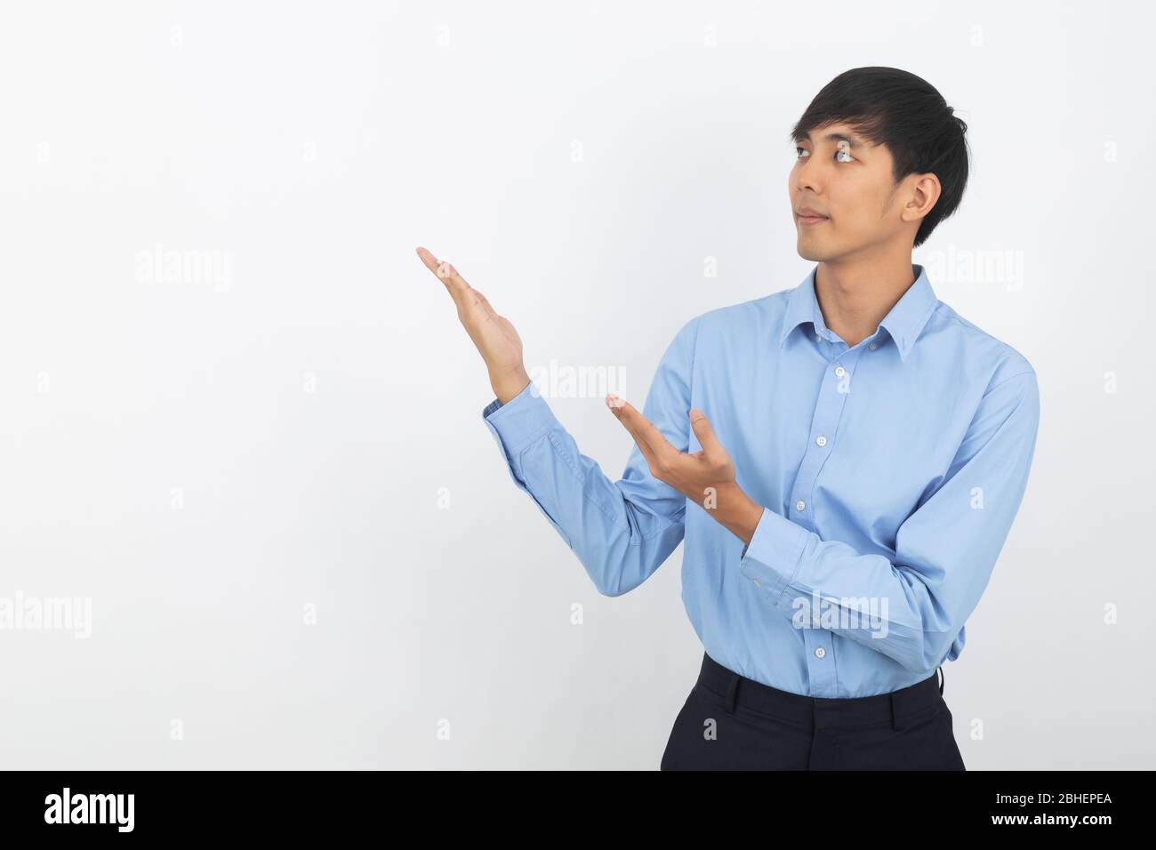 Young asian business man with blue shirt pointing to the side with hands to present a product or an idea while looking forward smiling isolated on whi Stock Photo