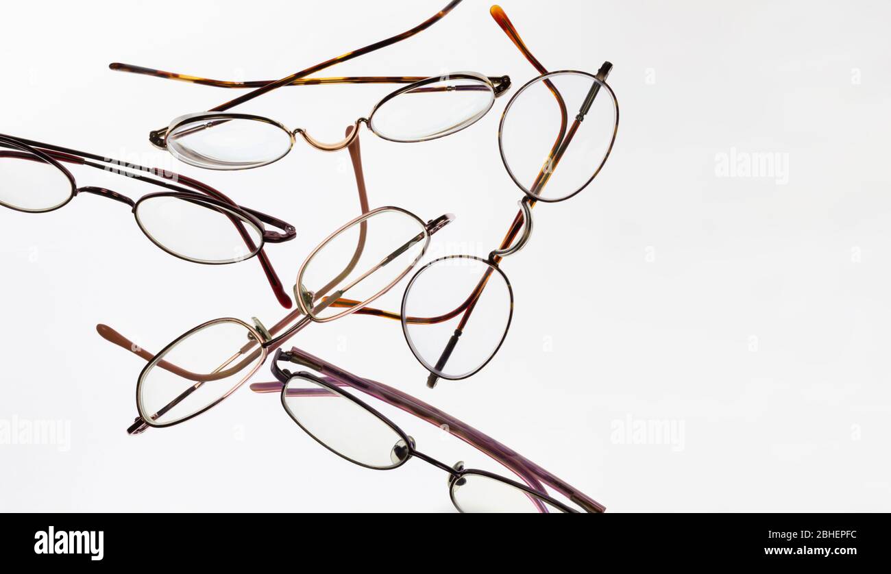 assortment of five pairs of metal or wire frame eye glasses arranged randomly on a soft white background. Copy space on right. Stock Photo