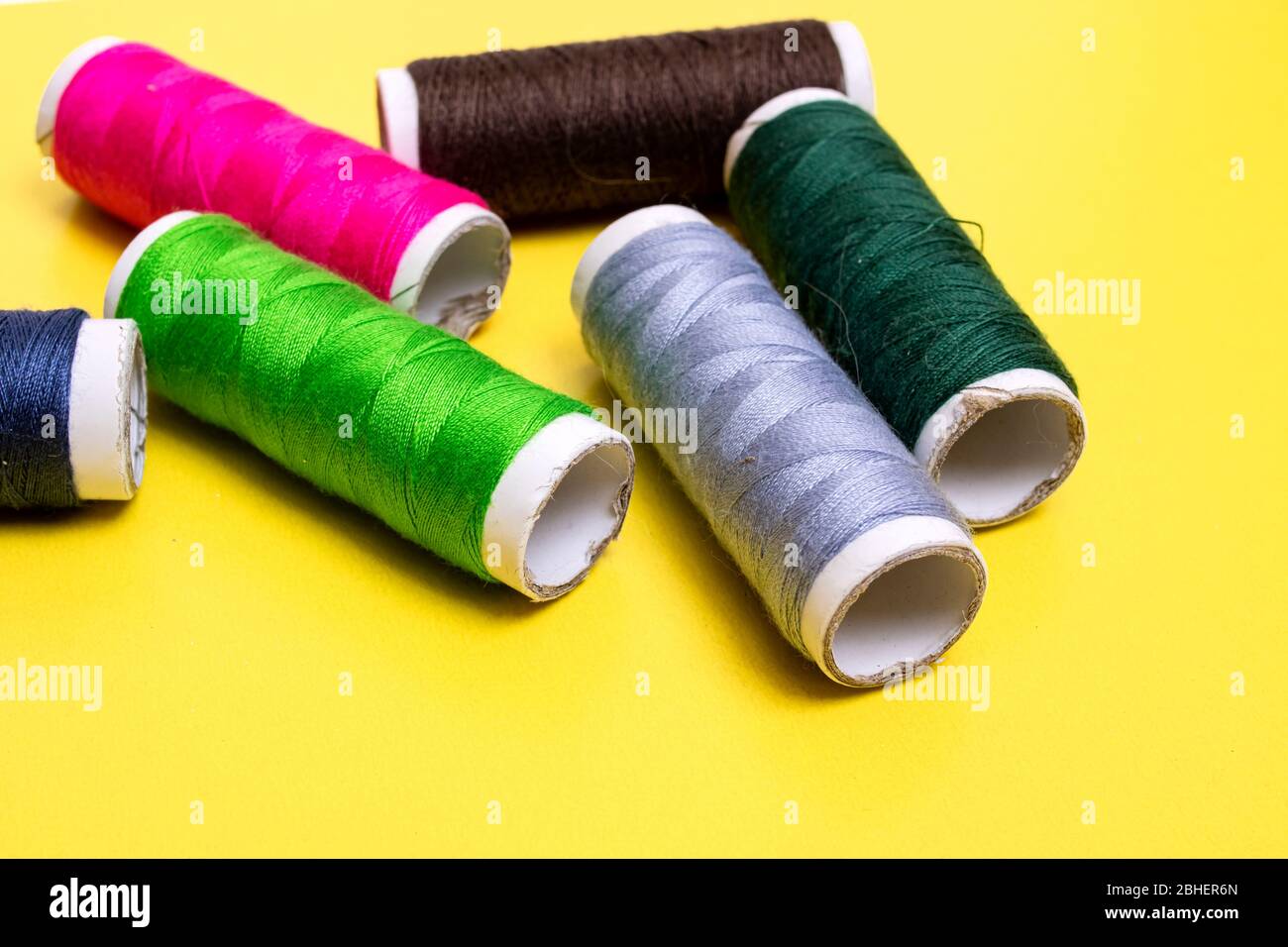 Coils with multicolored threads on yellow background Stock Photo