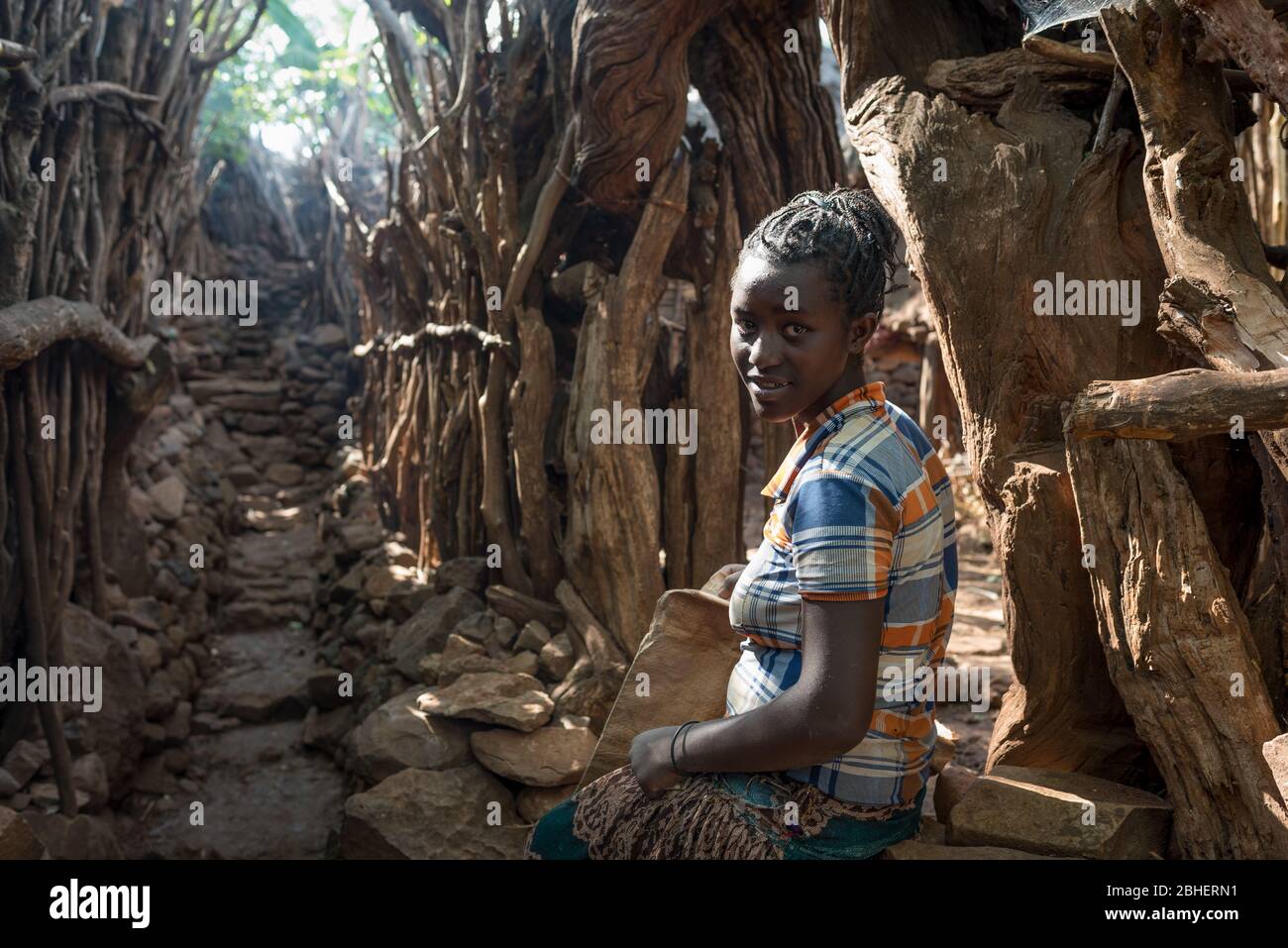 Young woman rests outside her family compound after climbing rocky village path,  Konso ethnic group or tribe, Mecheno village, Abra Minch, Ethiopia. Stock Photo