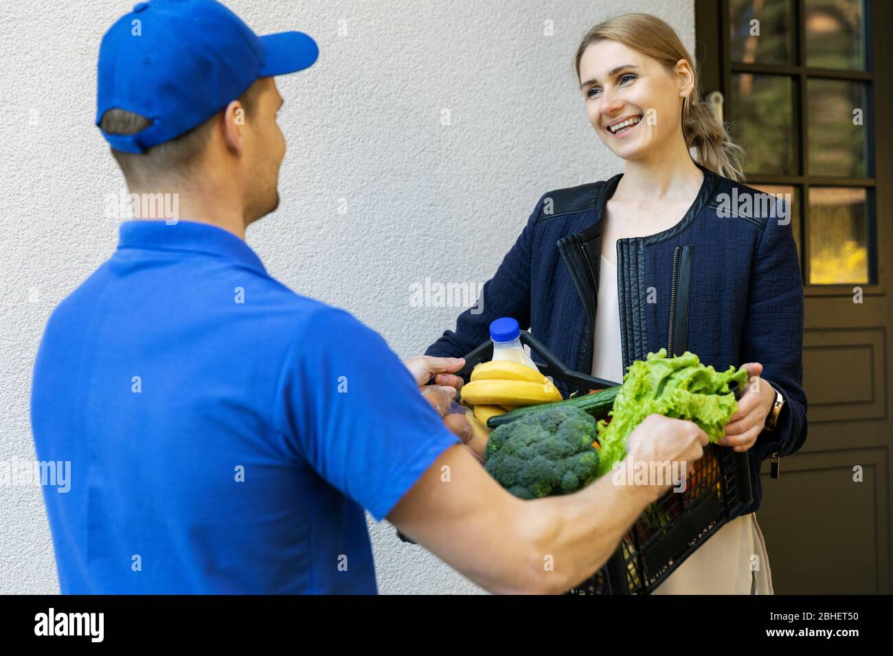 woman receive online grocery order box from delivery man at home Stock Photo