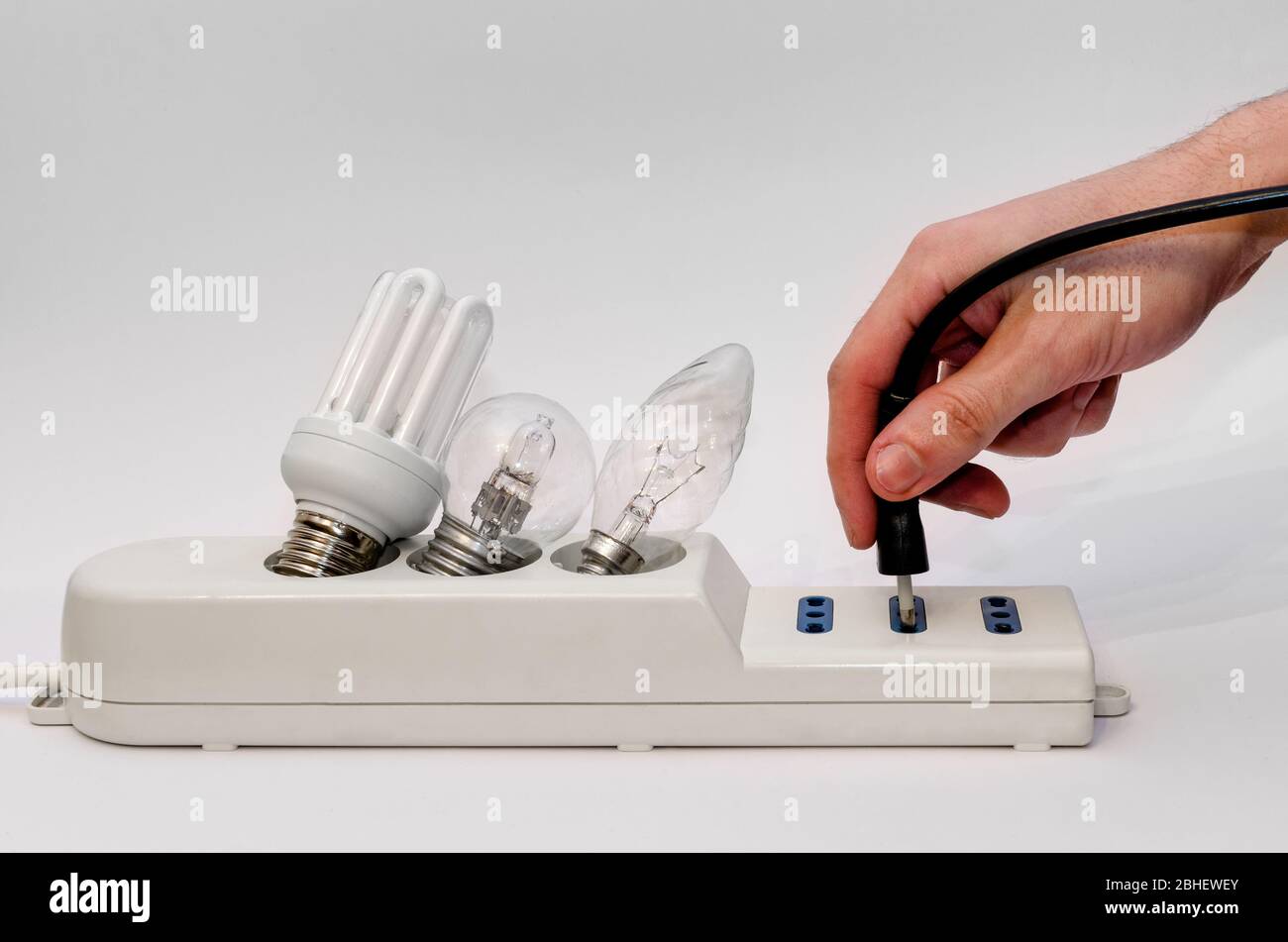 Power strip with three light bulbs of different type, white background and an hand holding a plug Stock Photo