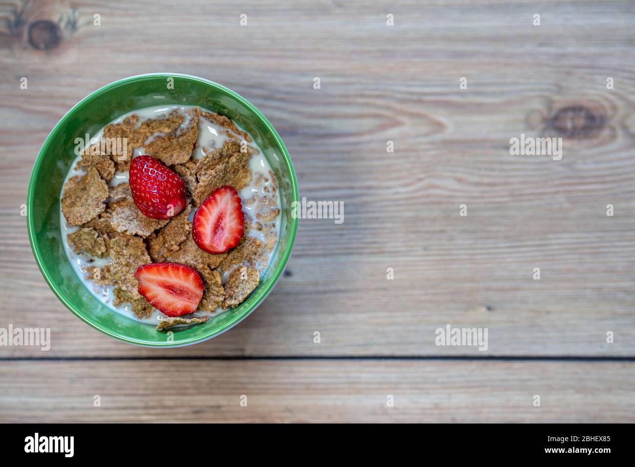 Top view of Healthy Whole-Grain Cereals Fitness meal. Milk, strawberries and Cereals breakfast. Green bowl on wooden kitchen table background Stock Photo