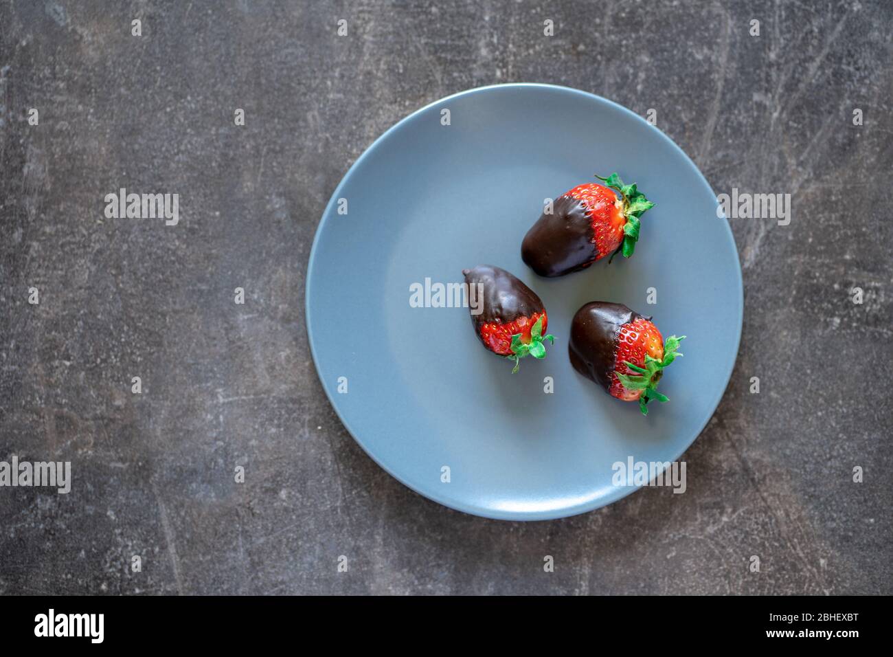 Top view of fresh healthy strawberries dipped in dark chocolate on a blue plate Stock Photo