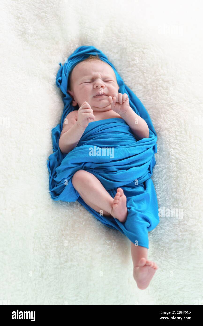 A small newborn girl in a blue diaper winced at the pain in her stomach. Cramp Stock Photo