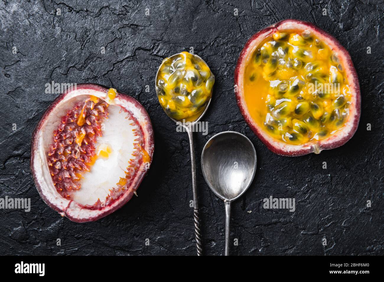 Slised passion fruit with silver spoons on black concrete background. Food photography Stock Photo