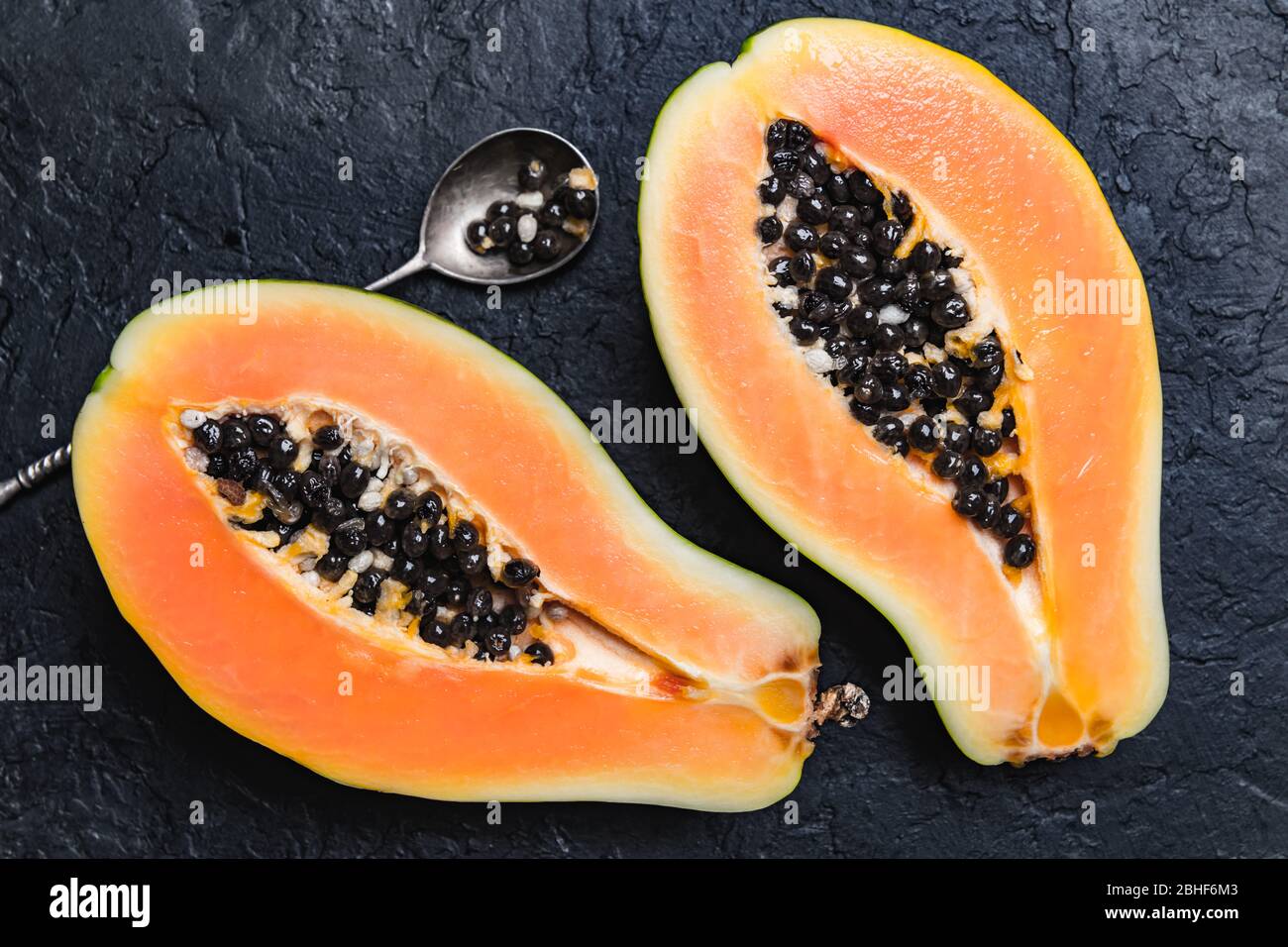 Slised papaya with silver spoon on black concrete background. Food photography Stock Photo