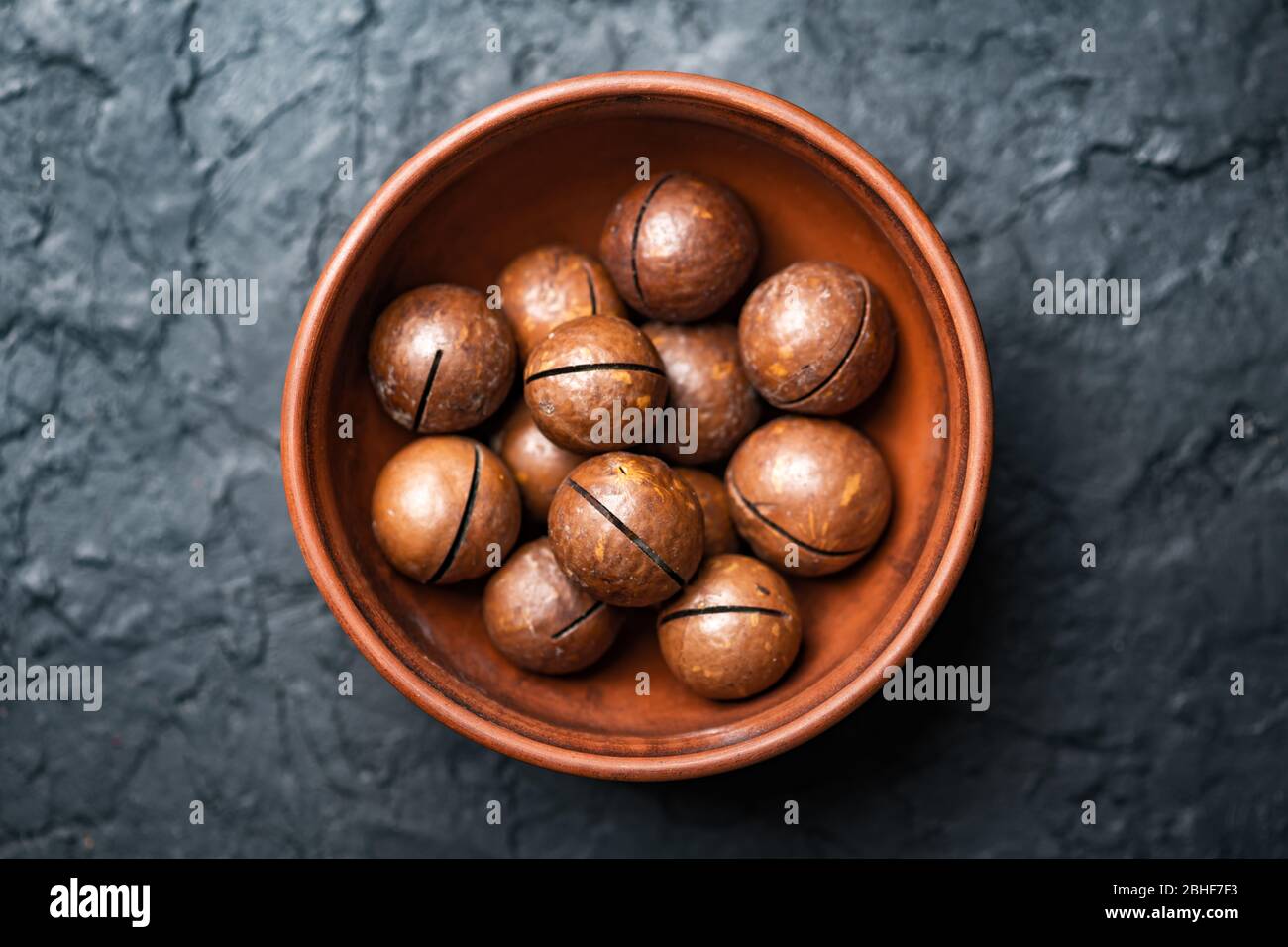 Dried organic Macadamia nuts in orange ceramic bowl closeup. Studio macro shoot. Black concrete background Stock Photo