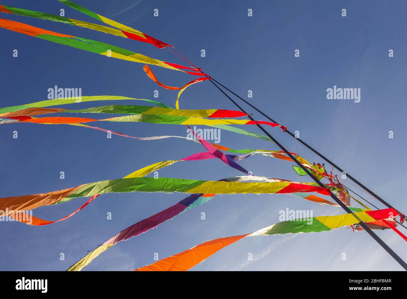 Colorful ribbons hanging on poles on blue sky background kite festival Stock Photo