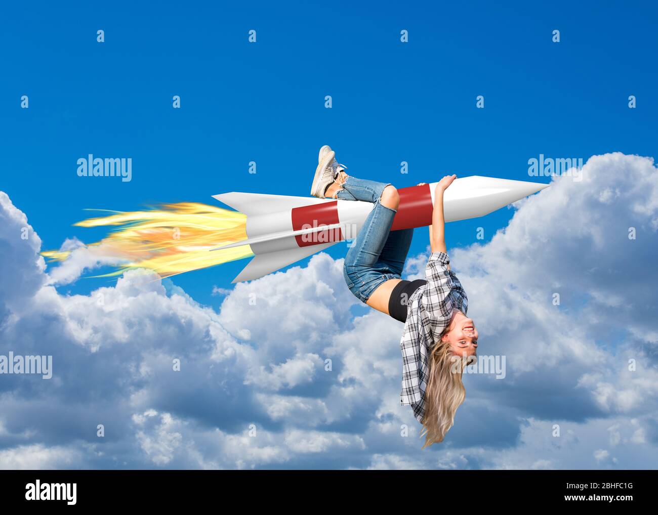 Young woman hangs on a rocket and flies with it through the clouds Stock Photo