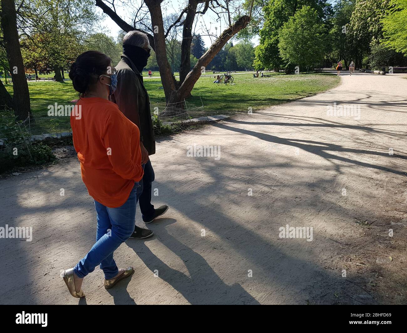 Old couple / grandparents ( man / male & woman / female ) wearing face mask ( surgical mask ), walking through park - covid -19 corona  virus lockdown Stock Photo