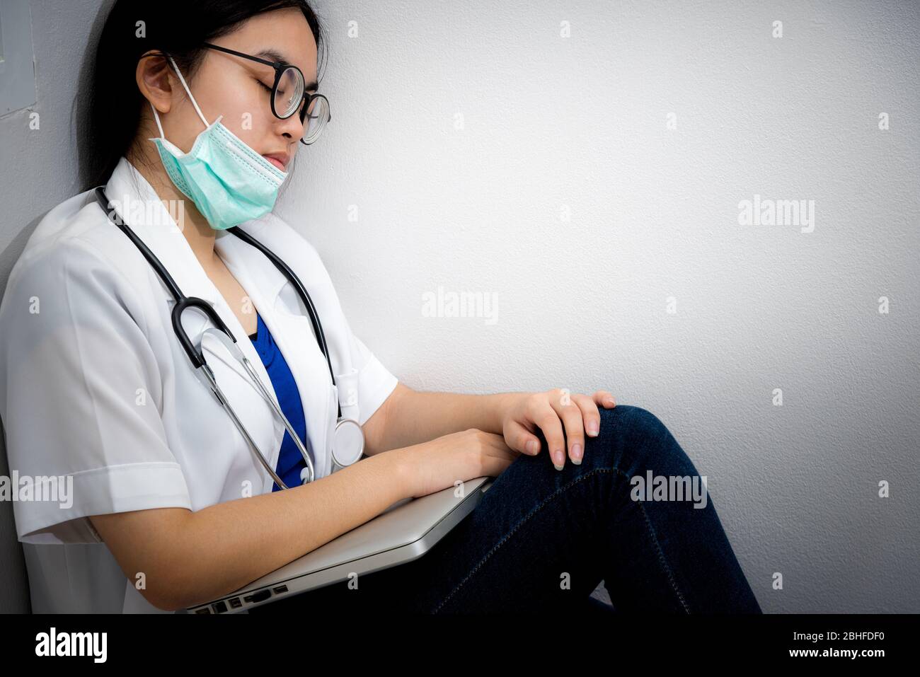 Asian young woman doctor wear mask to safety Coronavirus sit on the corner floor sleeping with exhaustion from overwork concept take care yourself is Stock Photo