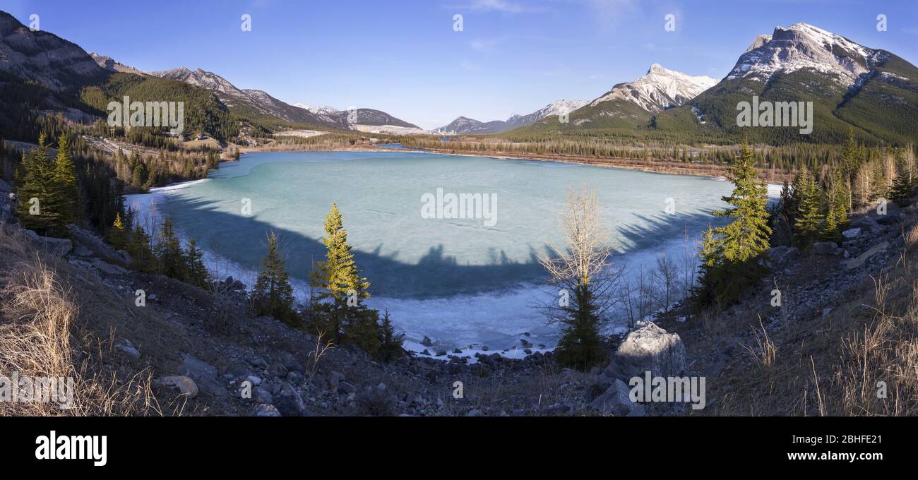 Frozen Ice Covered Rocky Mountain Gap Lake Bow Valley Scenic Panoramic Landscape View.  Distant Alberta Foothills Canadian Rockies Banff National Park Stock Photo