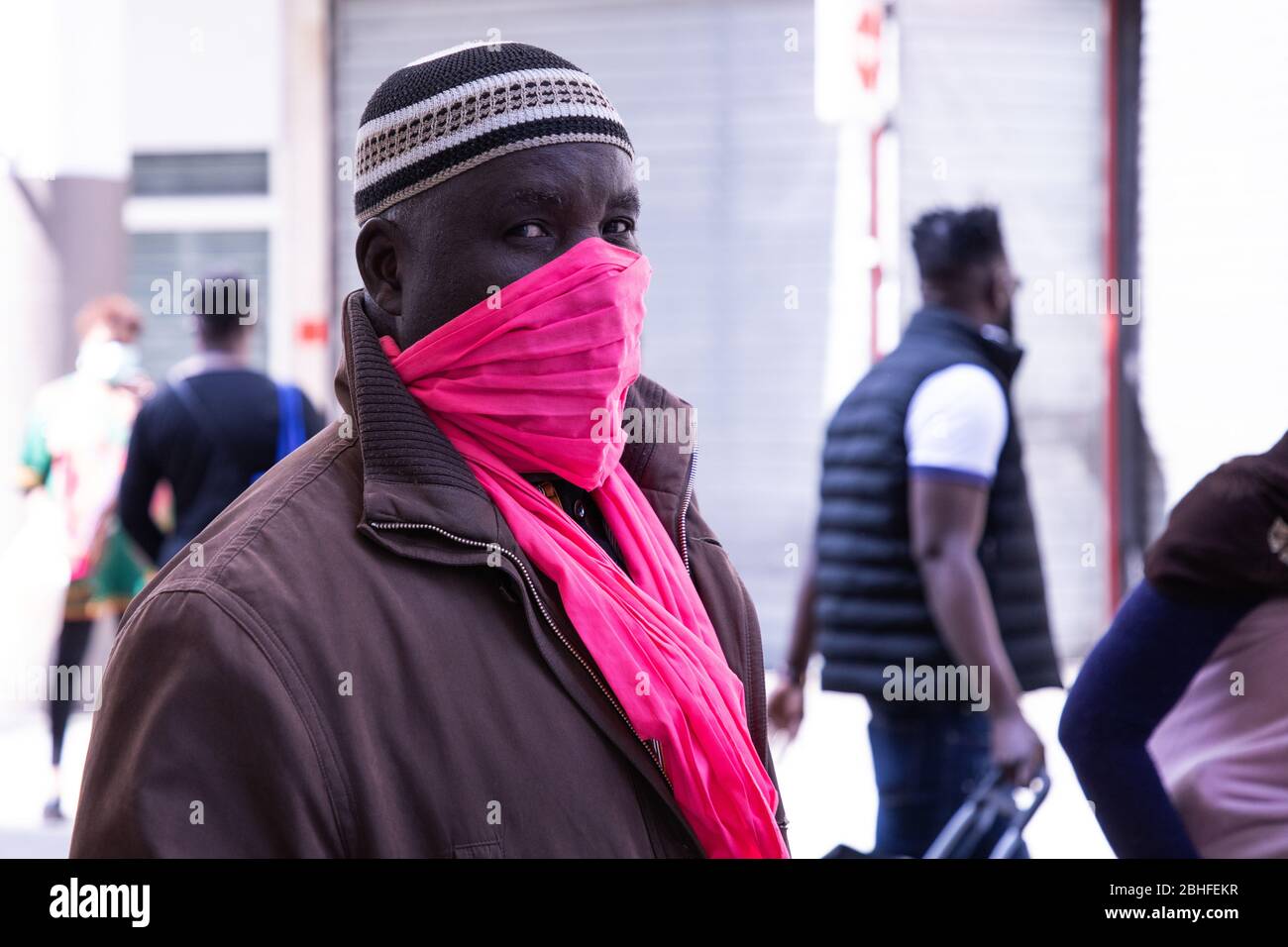 A Muslim man covering her mouth and nose with a scarf during Ramadan amid the corona virus pandemic.In Saint Denis, a Paris suburb where the population is predominantly Muslim, people line up at markets and butchers to prepare Ramadan meals in times of the pandemic. They wear masks to protect themselves from the virus, but social distancing is far from being fulfilled. Stock Photo