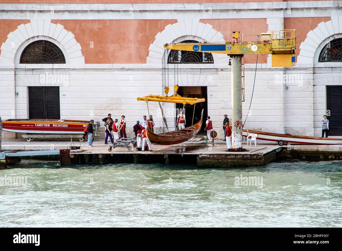 A gondola is lifted from the water to be moved into a storage building. People working. NMR; Unidentifiable people. Stock Photo