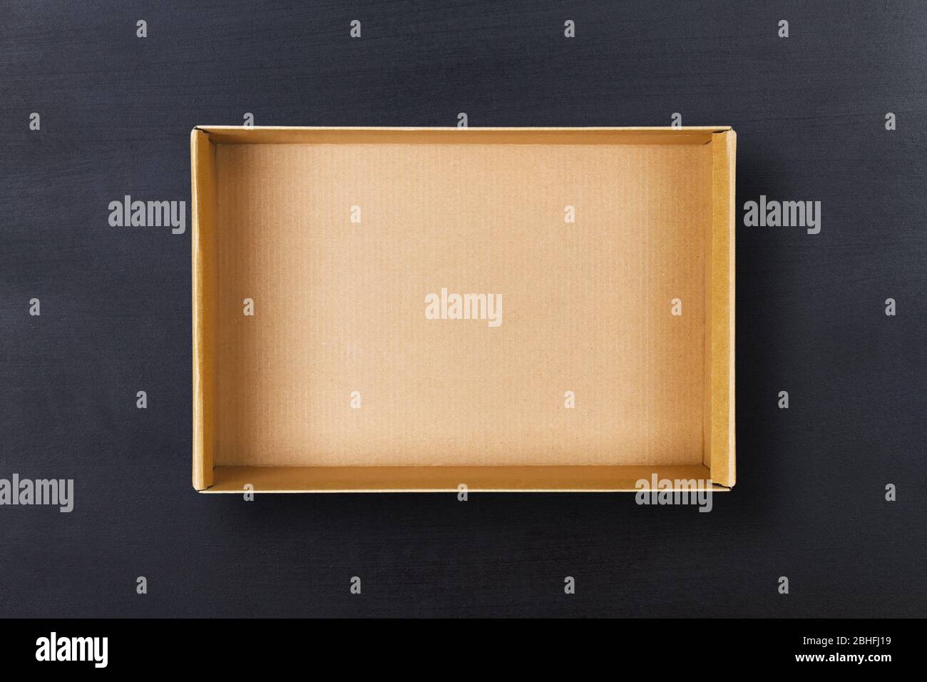 Open cardboard box on chalkboard background. Empty cardboard package on black texture Stock Photo