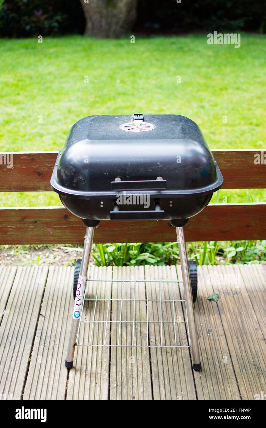 Full view of small compact barbecue grill with charcoal placed on patio with garden view Stock Photo