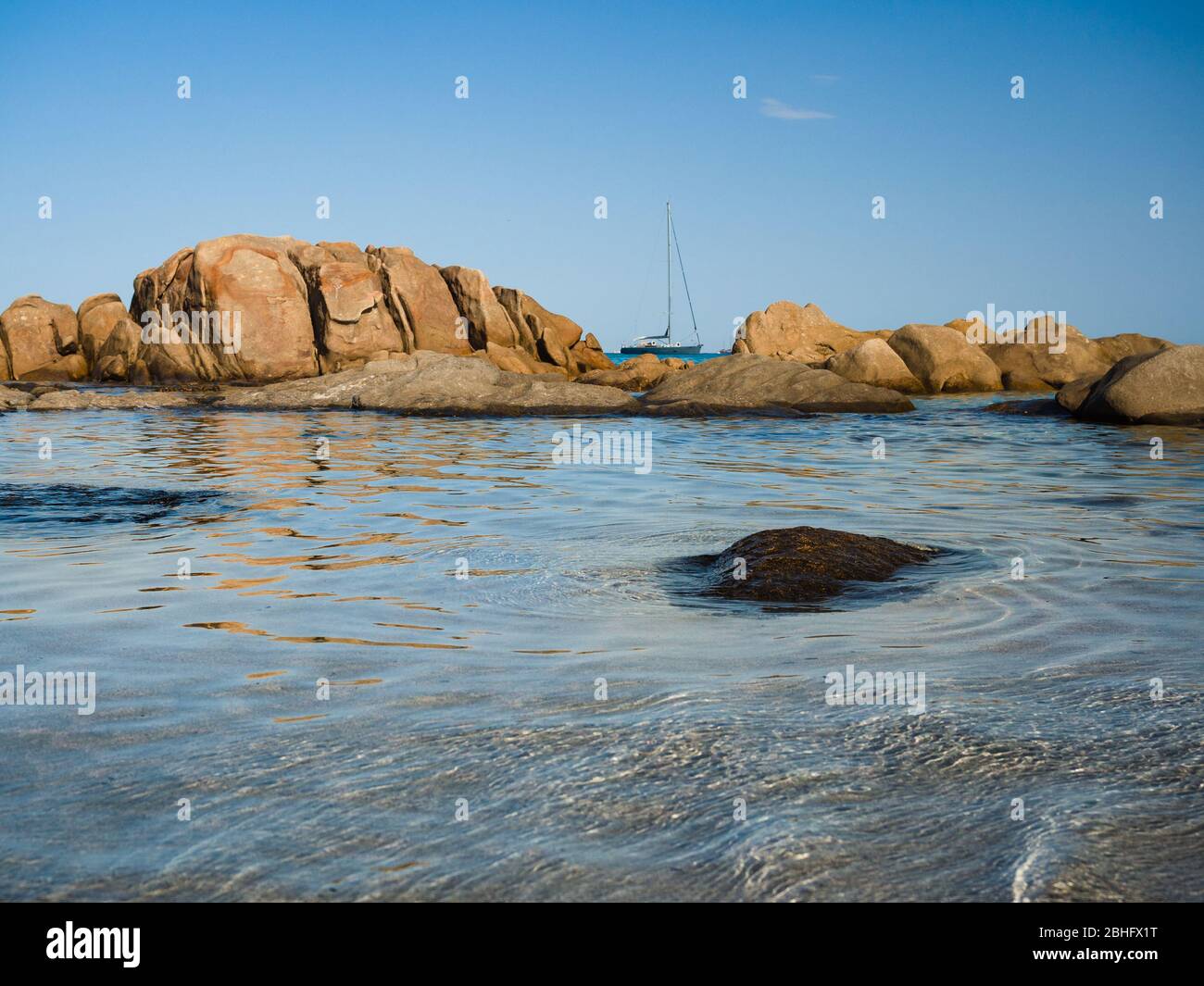 Sailboat sails near the coast and rocks of the transparent sea of Sardinia, Italy. Stock Photo