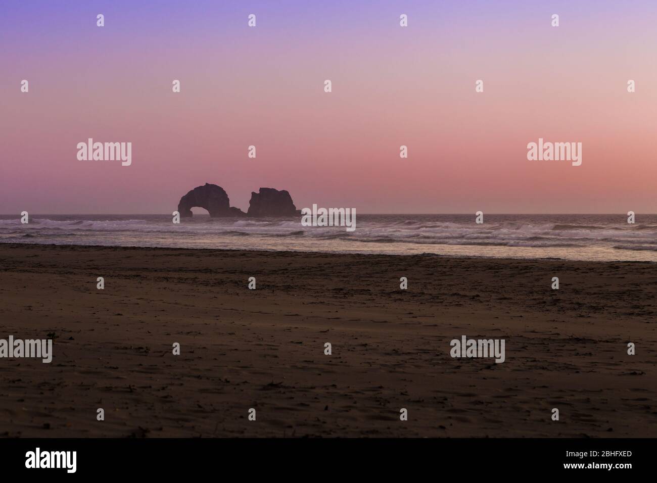 Oregon coast beach with a magnificent sunset with rocks in the distance in the ocean. Stock Photo