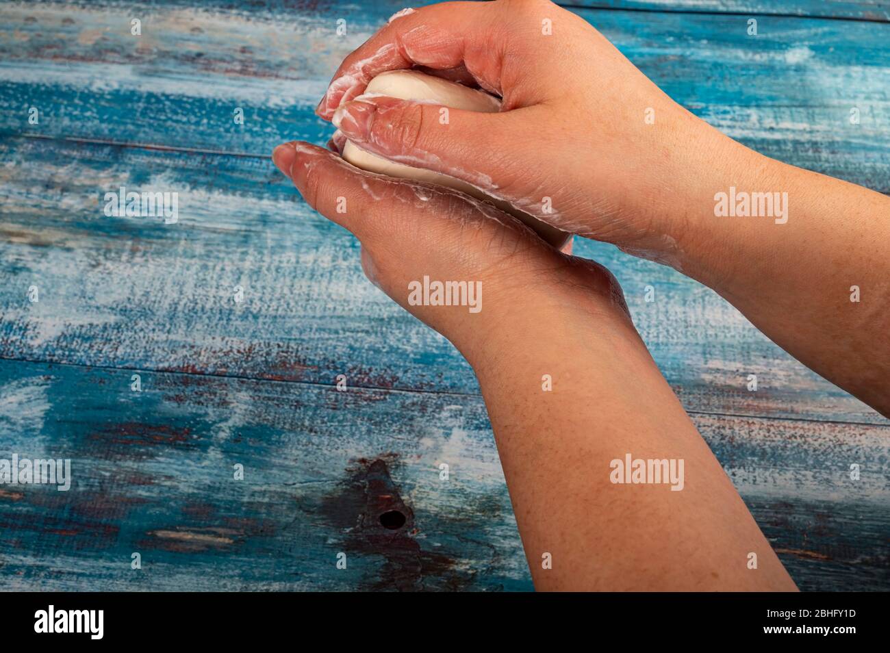 Someone is soaping their hands with a piece of toilet soap on a wooden background. Close up. Washing hands with soap is a prevention of COVID-19 infec Stock Photo