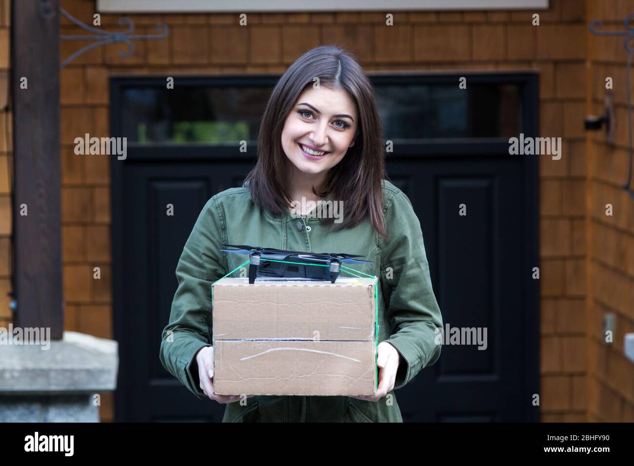 Attractive smiling young brunette woman holding a package that has been delivered by an autonomous drone. Stock Photo