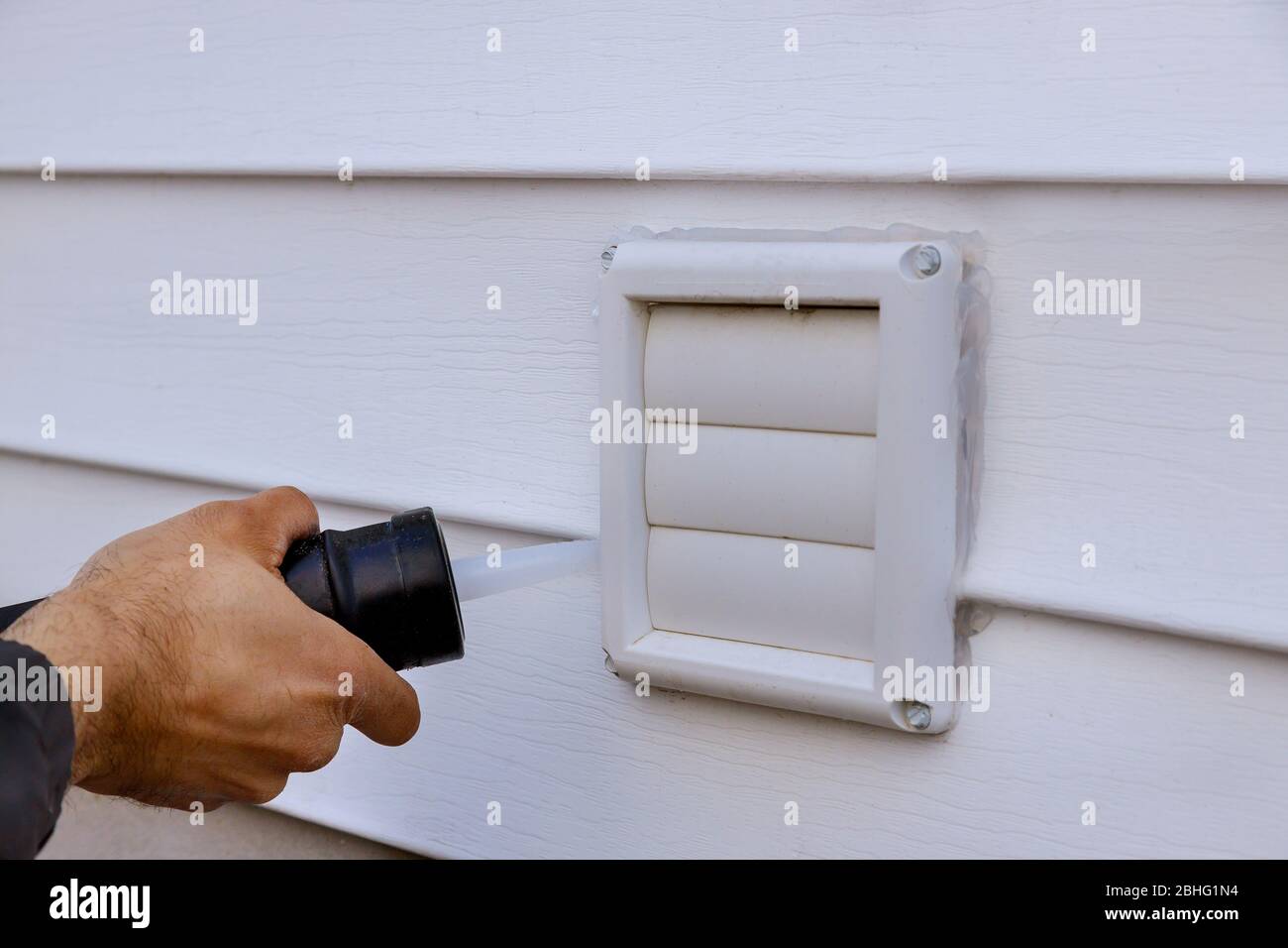 Applying silicone on plastic exhaust fan on the wall outside siding