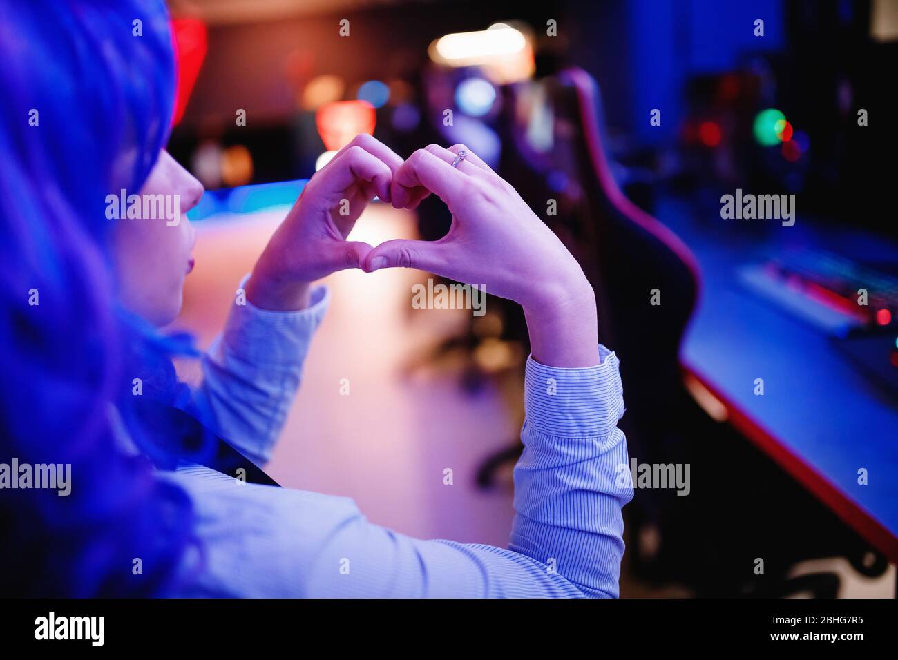 Streamer beautiful woman shows heart sign with hands professional gamer playing online video games computer, neon color Stock Photo