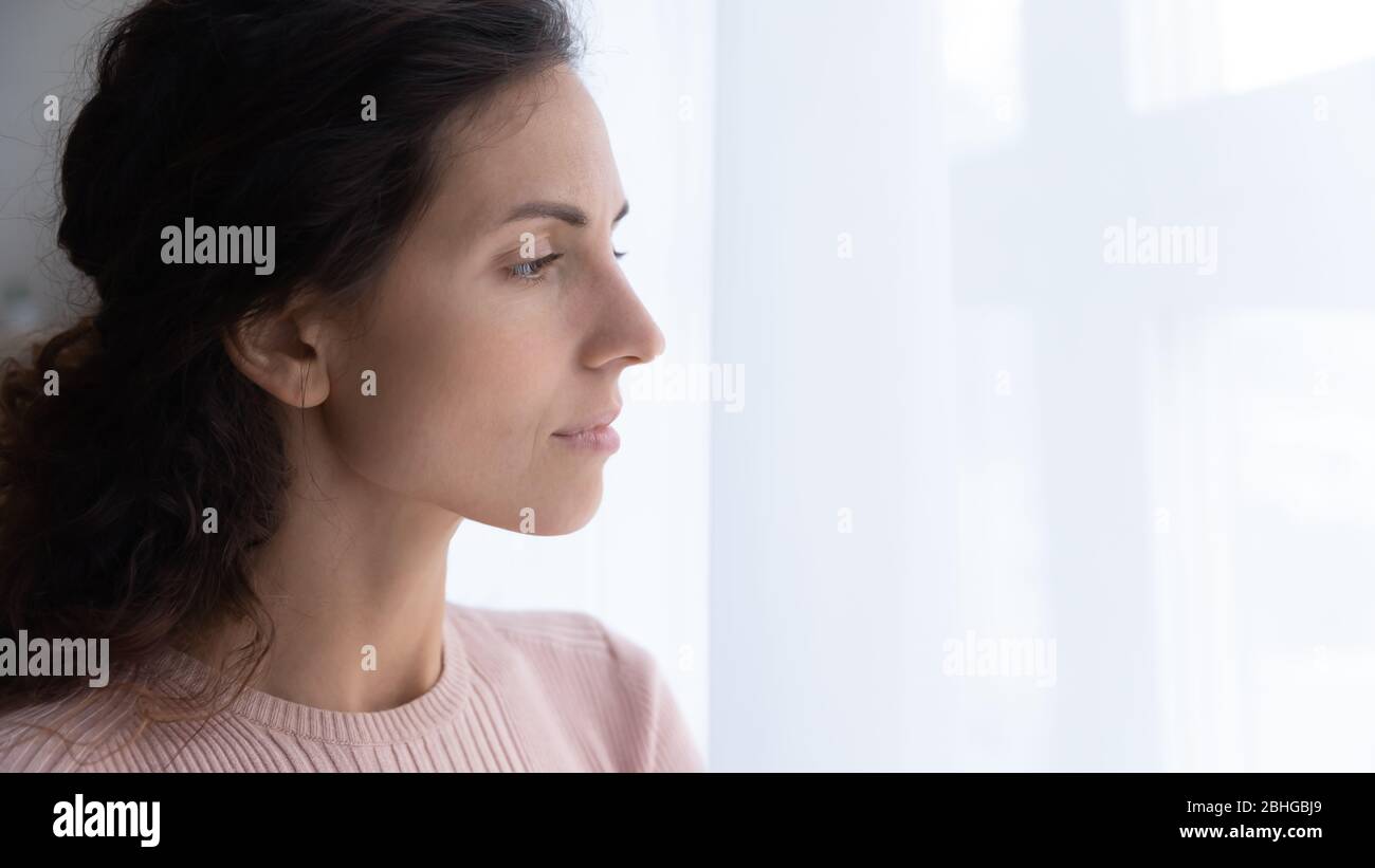 Thoughtful young woman looking away through window. Stock Photo
