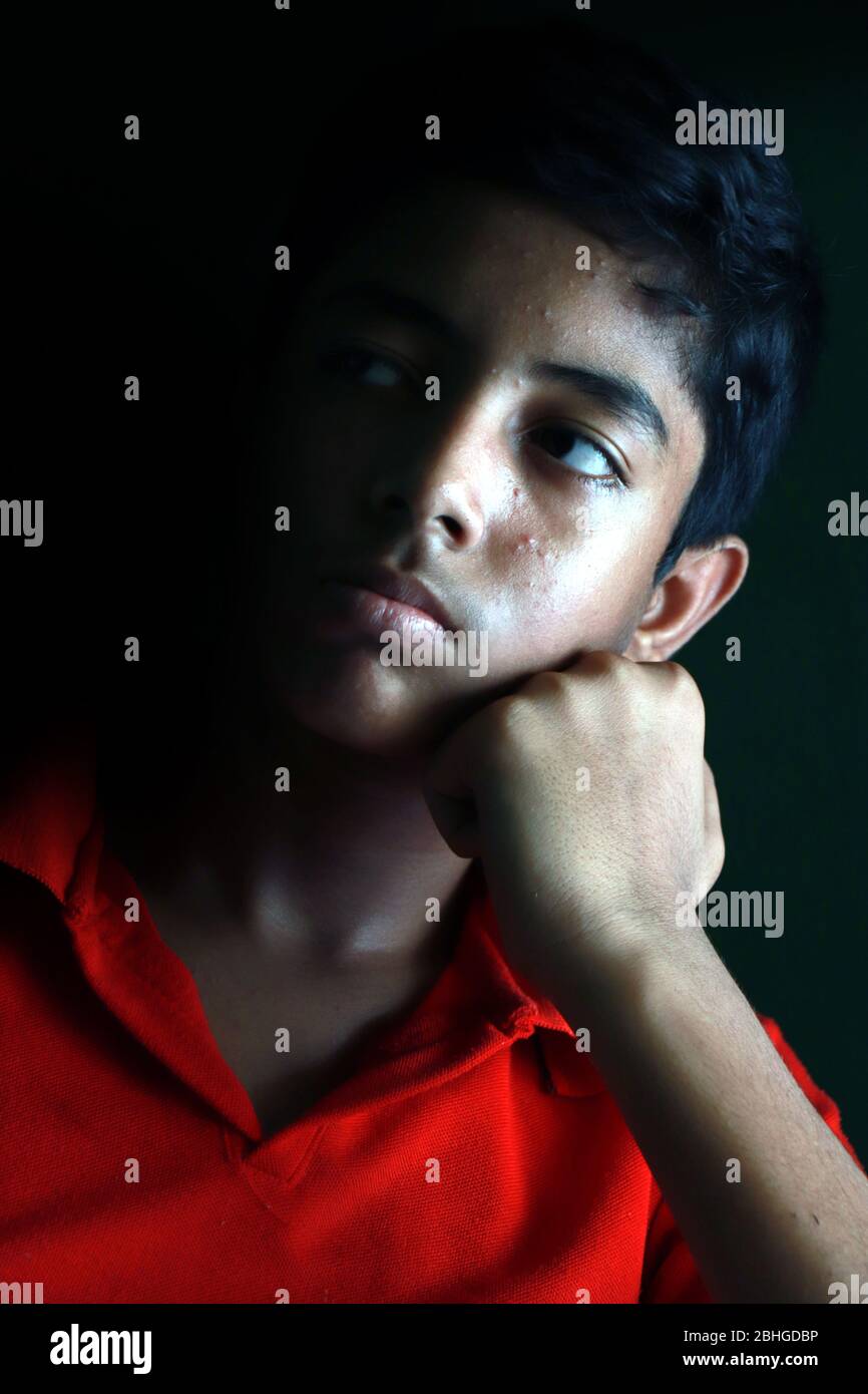 Portrait of a stressed Asian boy in front of black background. An Indian melancholy boy is thinking. Sadness expression of an Asian boy. Stock Photo