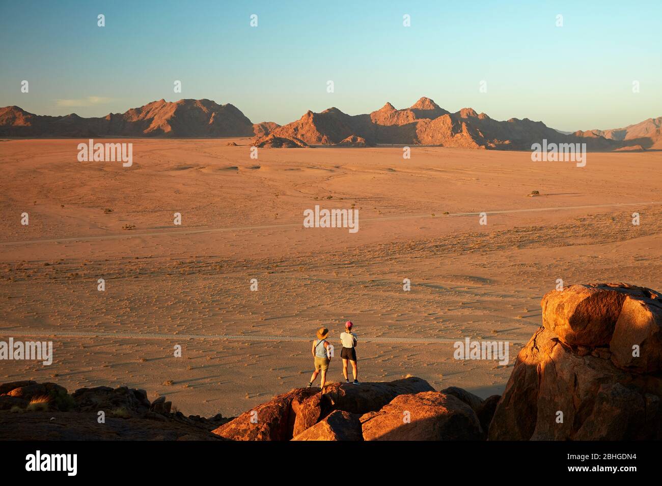 Women looking at view of mountains from high on a rock koppie above Desert Camp, Sesriem, Namib Desert, Namibia, Africa (model released) Stock Photo