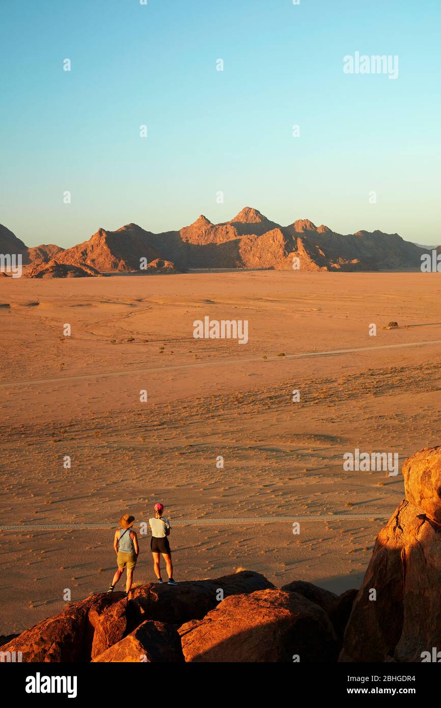 Women looking at view of mountains from high on a rock koppie above Desert Camp, Sesriem, Namib Desert, Namibia, Africa (model released) Stock Photo