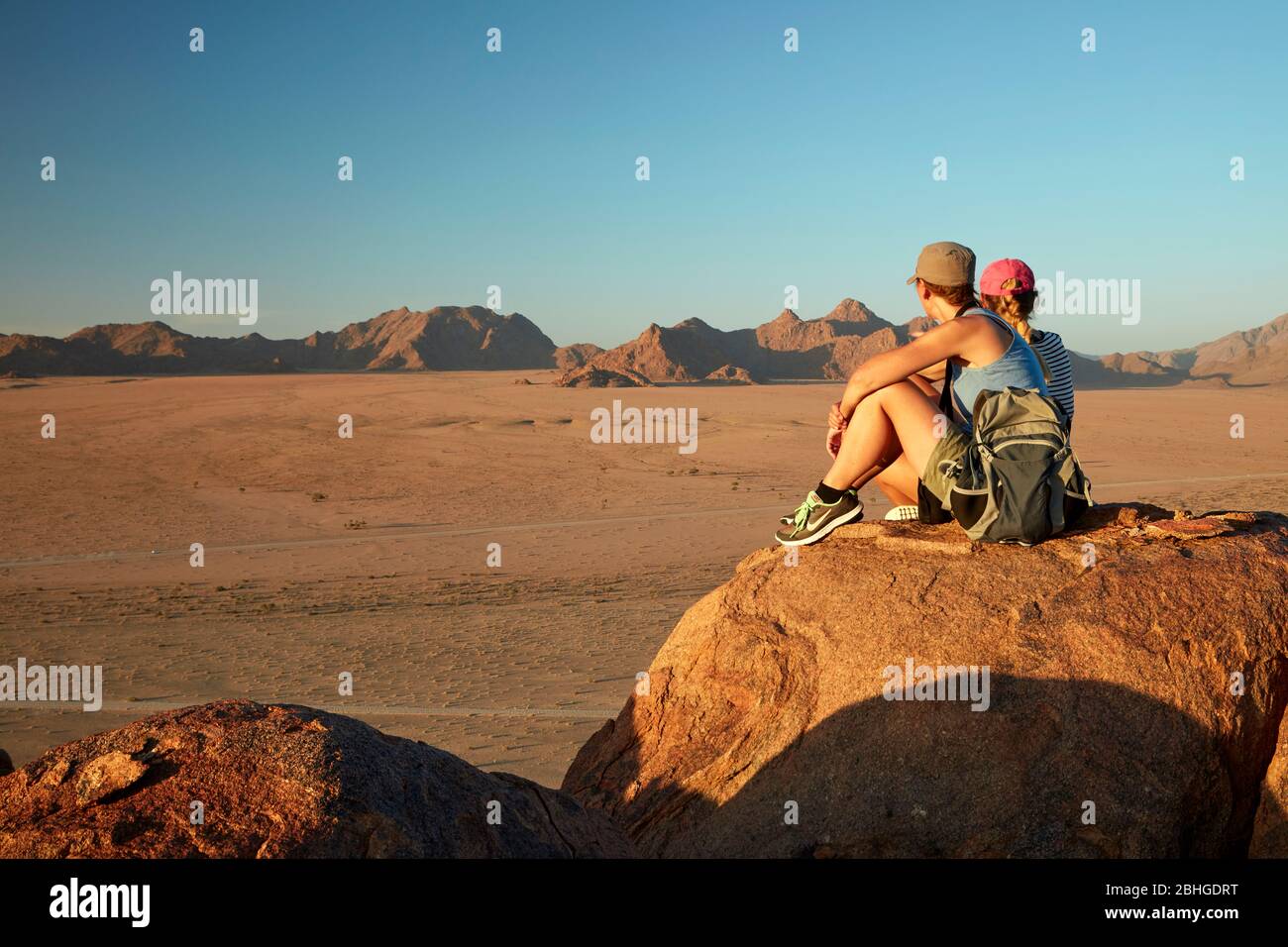 Women looking at view of mountains from high on a rock koppie above Desert Camp, Sesriem, Namib Desert, Namibia, Africa (model released) Stock Photo