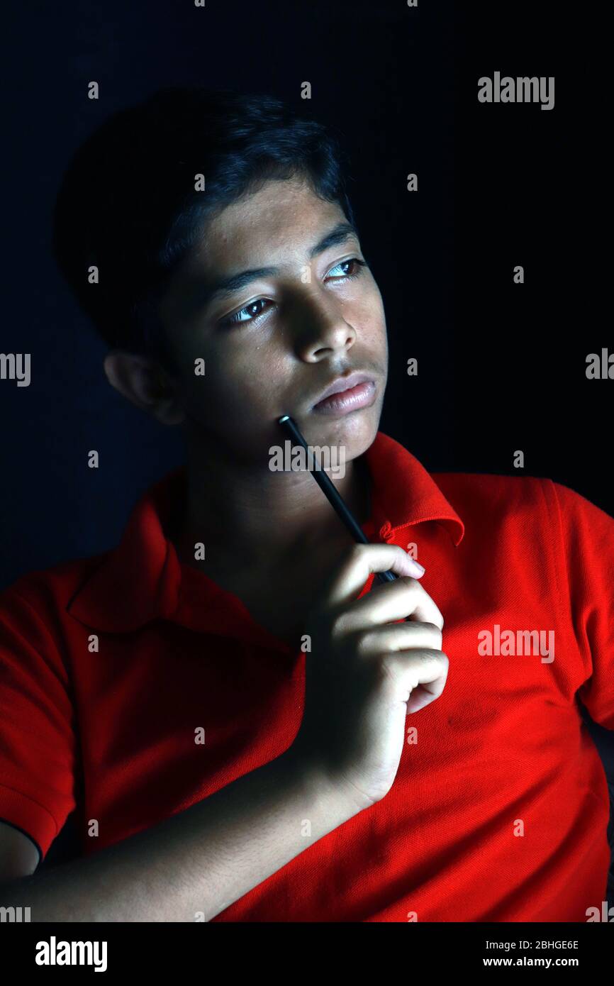 Portrait of a stressed Asian boy in front of black background. An Indian melancholy boy is thinking. Sadness expression of an Asian boy. Stock Photo