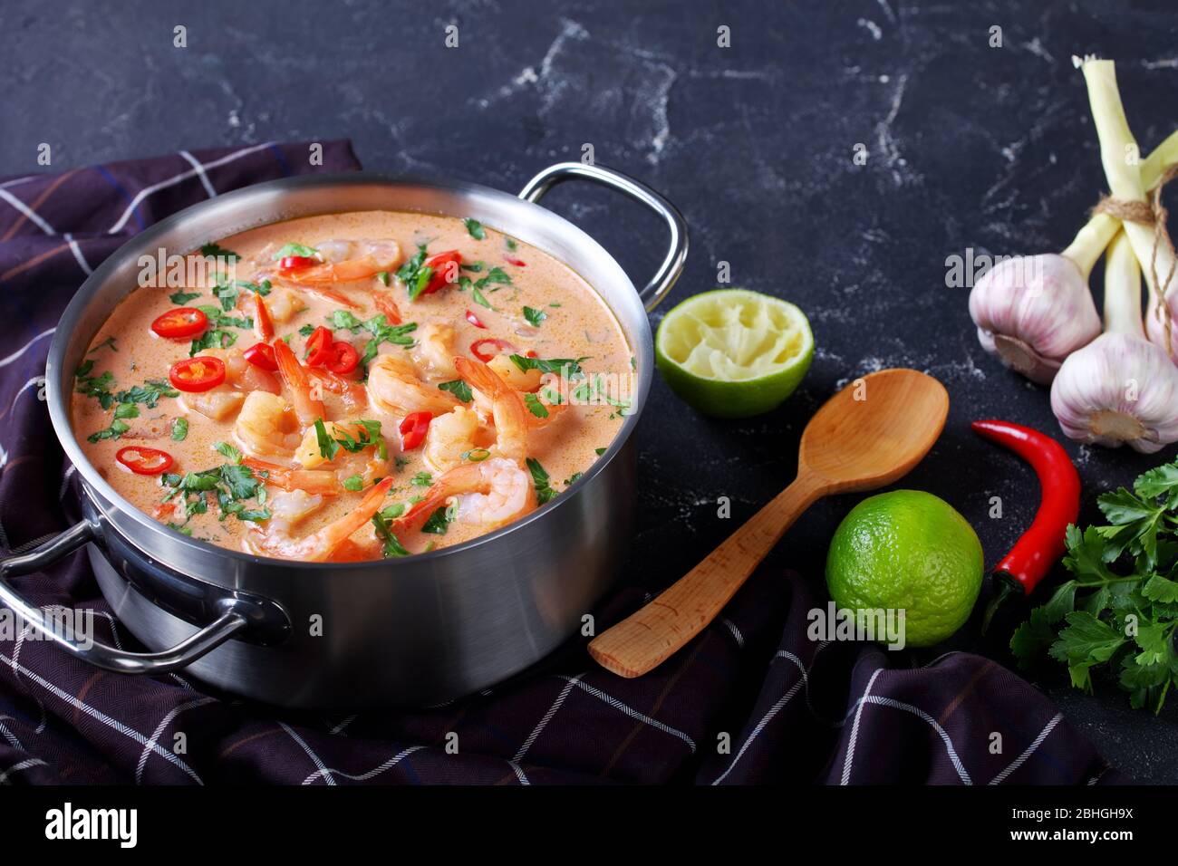 close-up of Tom Yum soup, tom kha soup in a saucepan on a concrete table with brown cloth and spoon, horizontal view from above, Stock Photo