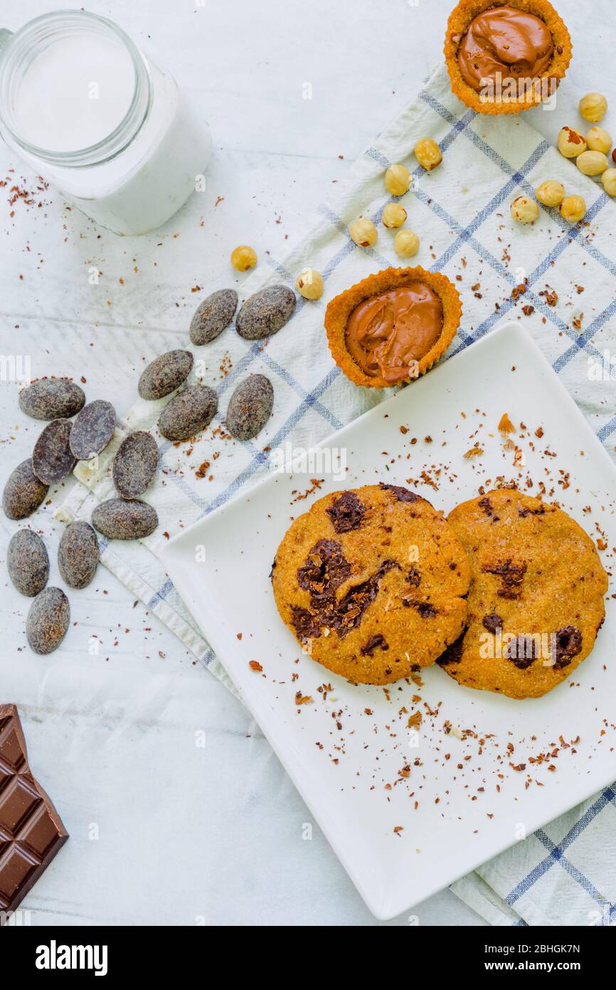Organic chocolate chip cookies with hazelnuts, coconut milk and chocolate candies in a square plate on a wooden table Stock Photo